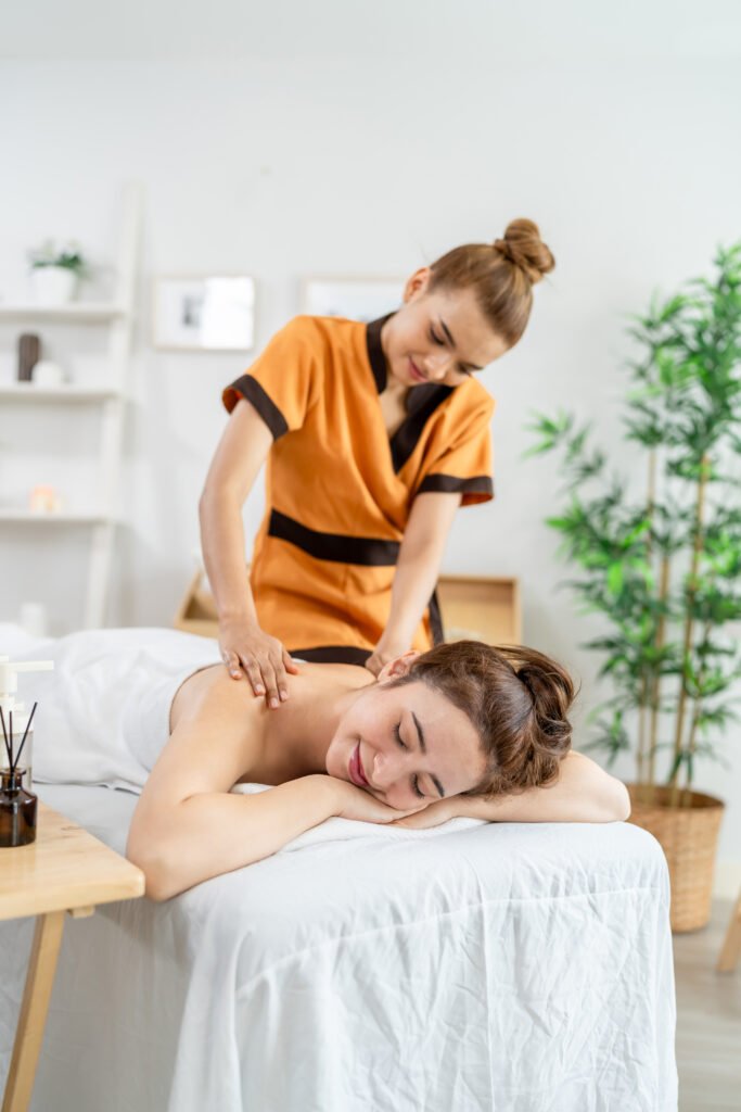 Beautiful woman getting back massage treatment with oil at beauty spa. Attractive young girl lying down on massage bed getting relaxing physiotherapy service from masseuse for body in spa clinic.